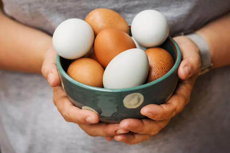 تعدادی تخم مرغ سفید و طلایی در کاسه سبز در دست یک دختر